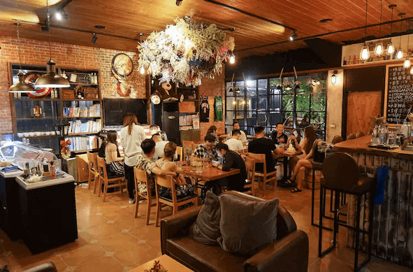 【美濃住宿】美濃煙城民宿的餐廳場景，位於民宿的公共區域。餐廳內裝飾著乾燥花和各種裝飾品，牆面同樣採用紅磚裸露設計，客人們正愉快地用餐，營造出溫馨的社交氛圍