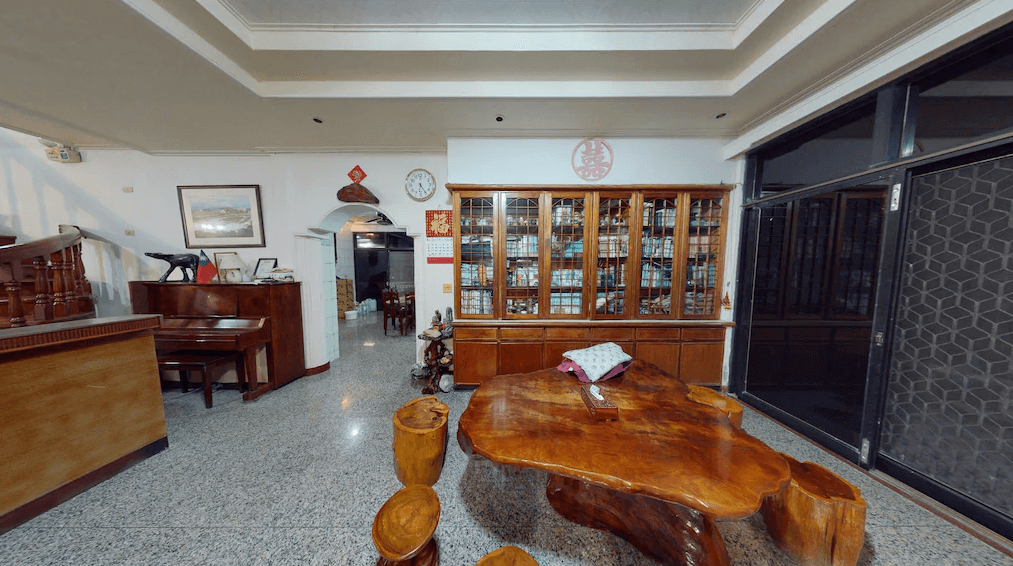 【美濃住宿】美濃百果園民宿的客廳，裝飾著木製家具和擺飾。客廳內有一架鋼琴、一張大理石桌和木雕椅，展示櫃內擺滿了收藏品，空間寬敞明亮，適合家庭聚會。