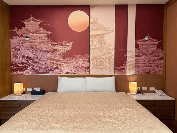 陽明山家新休閒會館豪華客房：一間設有東方風格壁畫的豪華客房，牆上描繪著古代建築和落日的圖案。房間內有一張鋪著白色床單和金色床罩的雙人床，旁邊有兩個床頭櫃和燈具，設計典雅且富有文化氣息