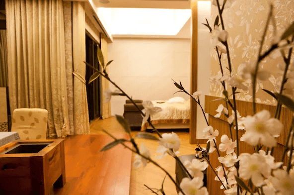 陽明山家新休閒會館套房：一間設有木質地板和豪華裝飾的套房，房間內有大型窗戶和絲質窗簾。背景是盛開的花卉，前景為一個木質茶几和沙發，營造出溫馨和舒適的居住環境