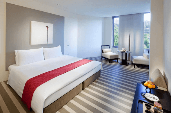 雀客藏居臺北陽明山豪華客房：一間現代化的豪華客房，設有一張鋪有白色床單和紅色床尾巾的雙人床。房間內的地毯為條紋設計，背景有簡約的掛畫，窗外可見綠色景色，旁邊有兩張休閒椅和茶几