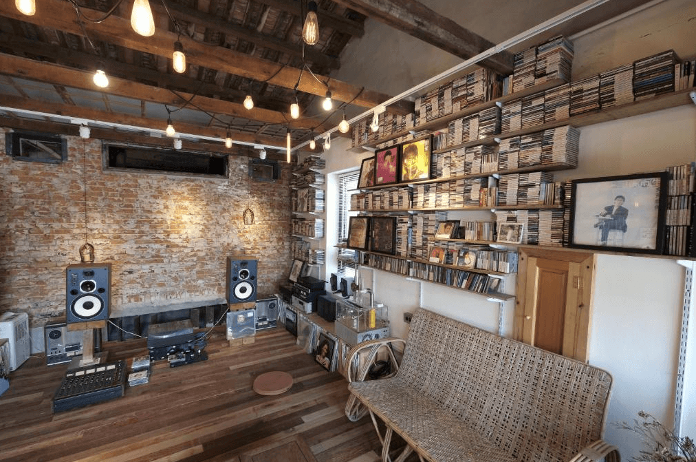 【美濃住宿】香蕉與黑膠三合院的休閒區，牆面採用裸露的紅磚設計，配有大量的音響設備和數百張黑膠唱片，頂部掛有暖色燈泡，營造出溫馨的氛圍，適合音樂愛好者放鬆和享受音樂。