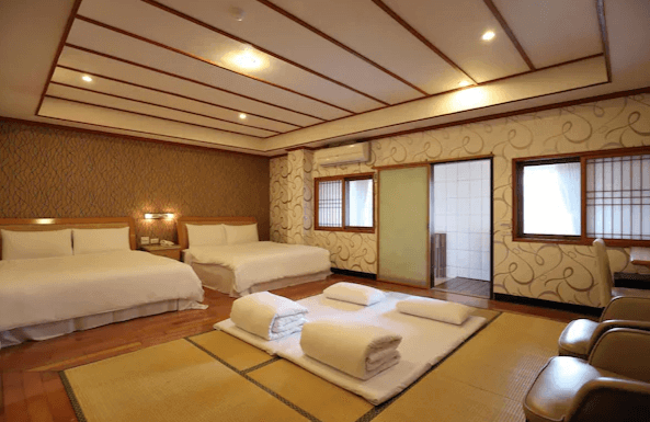 麗之湯溫泉會館家庭房：一間寬敞的家庭房，內有兩張雙人床和榻榻米區域，提供充足的休息空間。房間內設計典雅，牆壁上有精美的圖案，適合家庭入住，旁邊還有一個小型浴室，方便客人使用