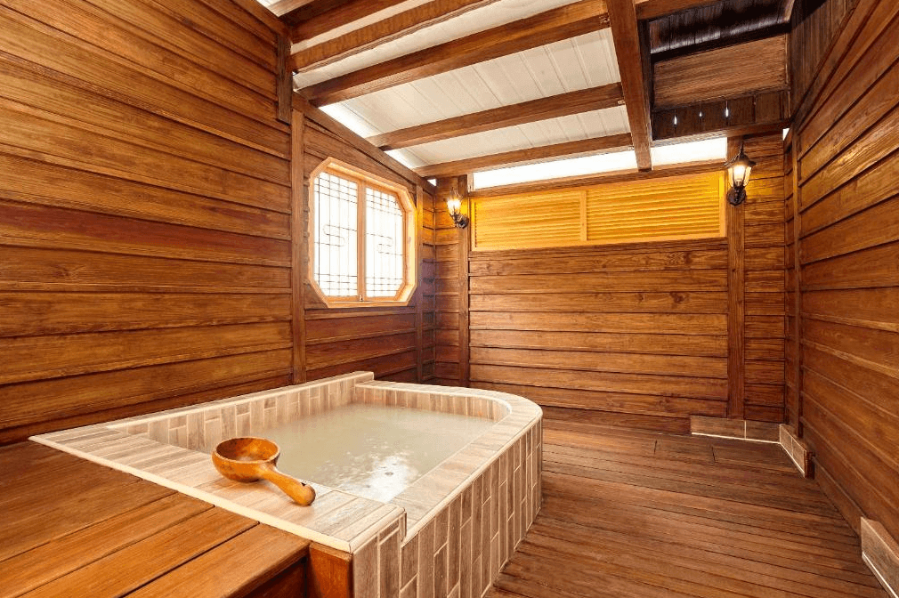 麗之湯溫泉會館木質溫泉浴池：一間設有木質牆壁的私人溫泉浴池，內部由石材構成，設計典雅且自然。浴池旁邊擺放著木質水勺，提供舒適和放鬆的泡湯環境