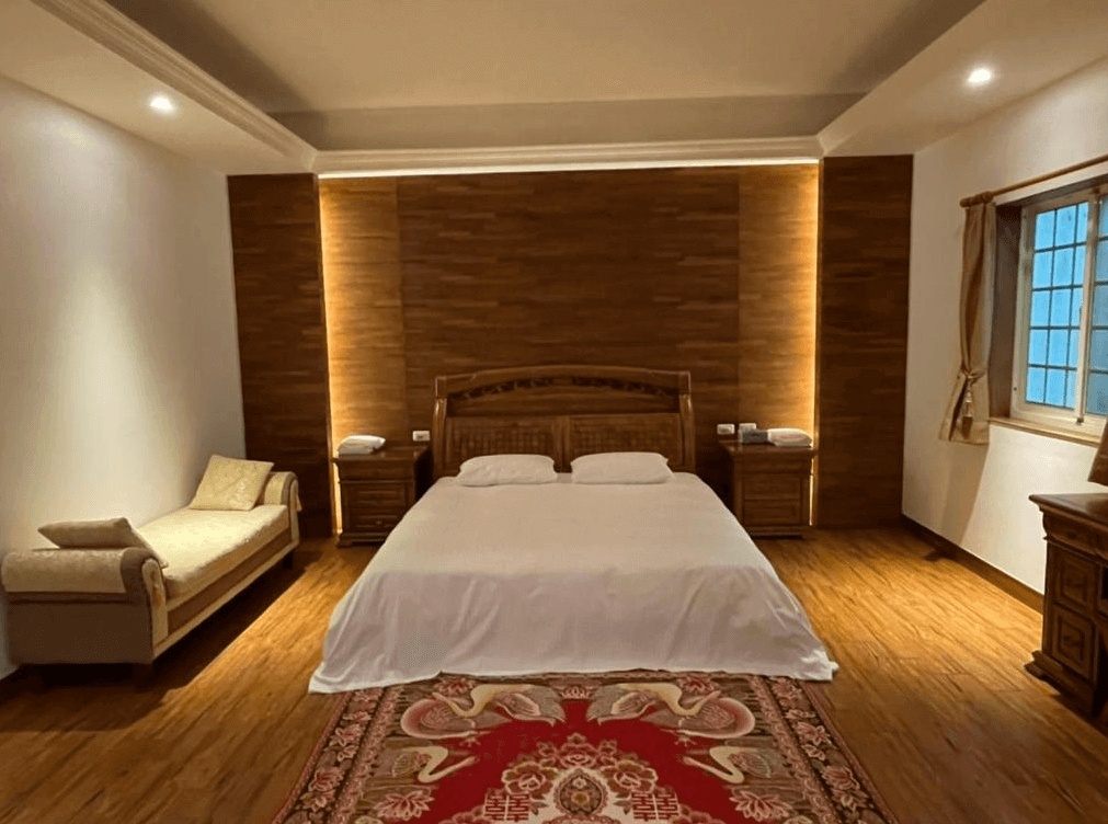 【九份寵物友善住宿】九份金瓜石樹屋的豪華雙人房，房間內設有一張大雙人床，兩側各有一個床頭櫃。床尾側放置了一張舒適的長椅，牆面以木質板材裝飾，呈現溫暖的氛圍。