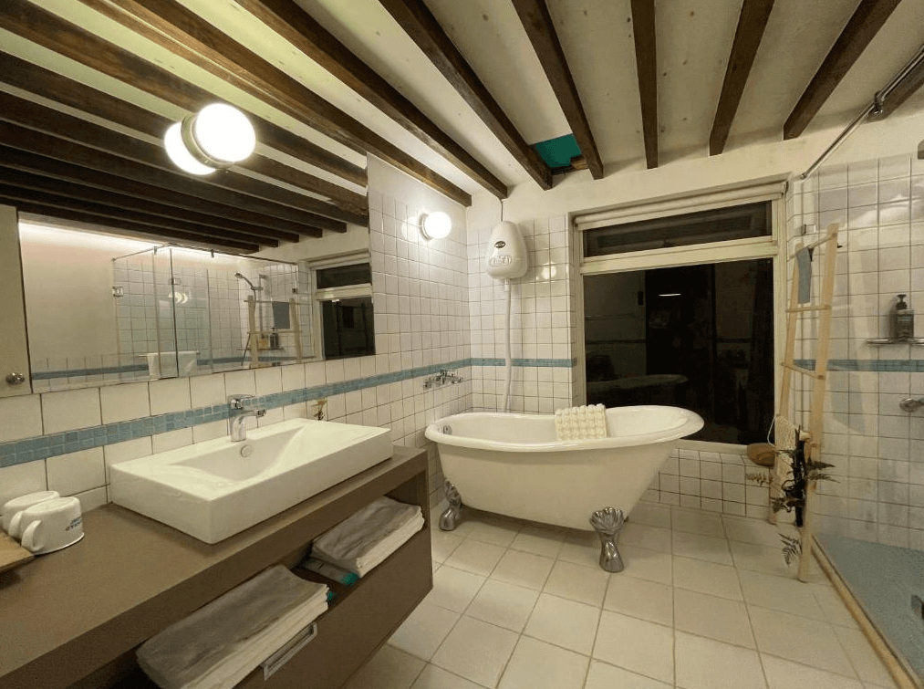 【九份寵物友善住宿】九份金瓜石樹屋的豪華浴室，設有獨立的浴缸和寬敞的洗手台。天花板上有木質橫樑，牆面以白色瓷磚裝飾，浴室整體設計典雅且具現代感。
