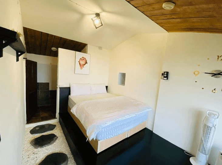 【九份寵物友善住宿】九居的舒適雙人房，內部設有一張大床，床下方以黑色平台支撐，牆上掛有一幅紅色花朵的畫。房間內有一個小浴室，地板上鋪有白色鵝卵石。