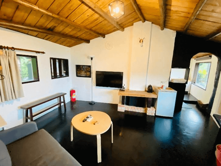 【九份寵物友善住宿】九居的溫馨客廳，內部設有一張舒適的沙發和一個小茶几，牆上掛有平面電視。天花板和家具以木質材料製成，房間內有充足的自然光線，設計簡約且溫暖。