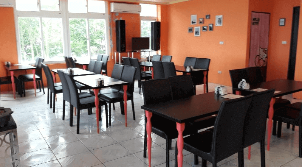 【九份寵物友善住宿】十三層民宿的用餐區，內部設有多組黑色桌椅，牆壁為橙色，充滿活力和溫暖的感覺。用餐區內光線充足，窗外可見綠意盎然的自然景觀，是享用美食的理想場所。