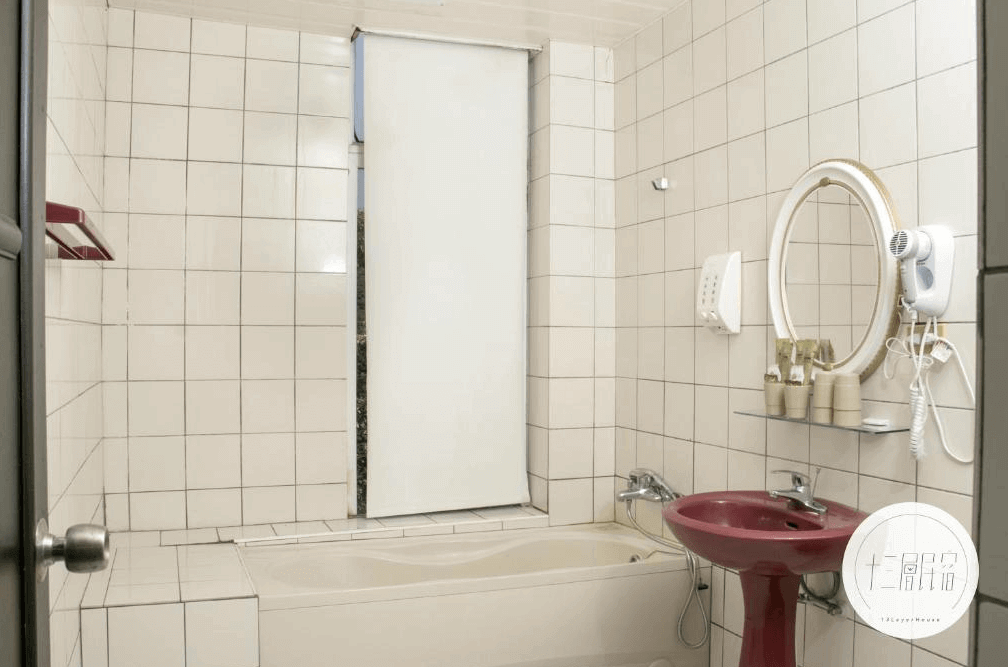 【九份寵物友善住宿】十三層民宿的浴室，牆面以白色瓷磚裝飾，設有一個浴缸和簡約的洗手台。浴室內配有一個圓形鏡子和吹風機，整體設計簡潔且實用，提供乾淨舒適的沐浴環境。