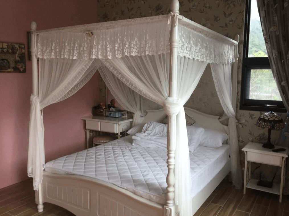 吾居吾素展示了一間浪漫的臥室，房間內設有一張四柱床，床上掛著白色的薄紗床幔，整體風格浪漫典雅。牆面和窗簾都採用了花卉圖案，增添了溫馨的感覺