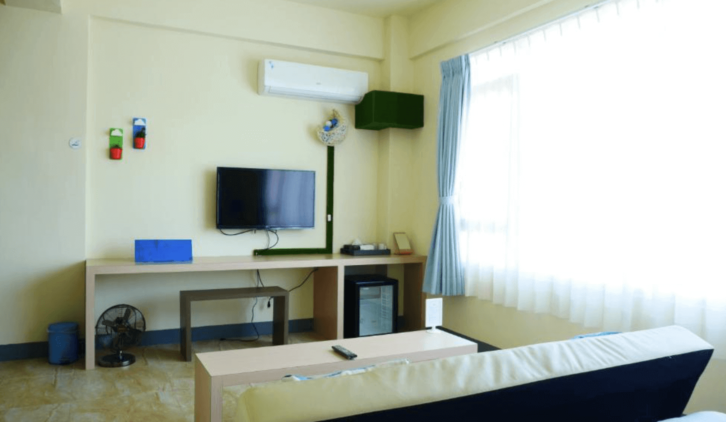 【池上民宿】最好的時光微旅宿的客房內設有電視和多功能書桌，讓客人可以輕鬆娛樂和工作。電視下方還有一個小冰箱，方便存放飲料和食物。房間內部布置簡潔，窗邊的藍色窗簾增添了一抹亮色，整體環境溫馨舒適