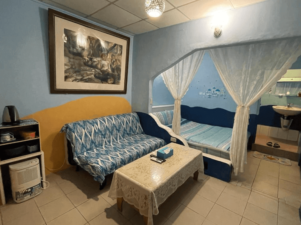 【九份寵物友善住宿】望幽谷民宿的溫馨客廳，內部設有一張帶藍色花紋的沙發和一張小茶几。沙發旁是帶有窗簾的床，牆上掛有一幅藝術畫，整體設計具有濃厚的家庭氛圍。