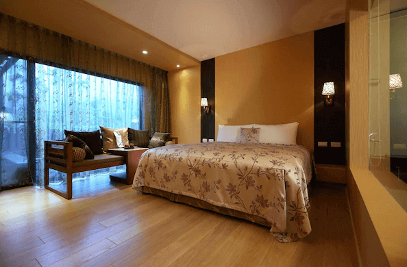 潭心閣民宿展示了一間溫馨的客房，房間內設有一張大床，床上鋪著花卉圖案的床單。床邊有兩盞牆壁燈，房間一角有一個舒適的休息區，窗外可以看到部分戶外景色