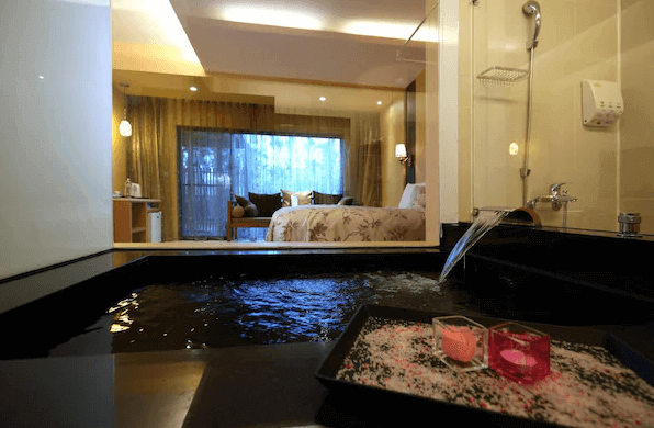 潭心閣民宿展示了一間帶有浴池的客房，浴池前景觀可以看到房間內的大床和休息區。浴池旁邊放置著幾個蠟燭和裝飾物，營造出浪漫的氛圍