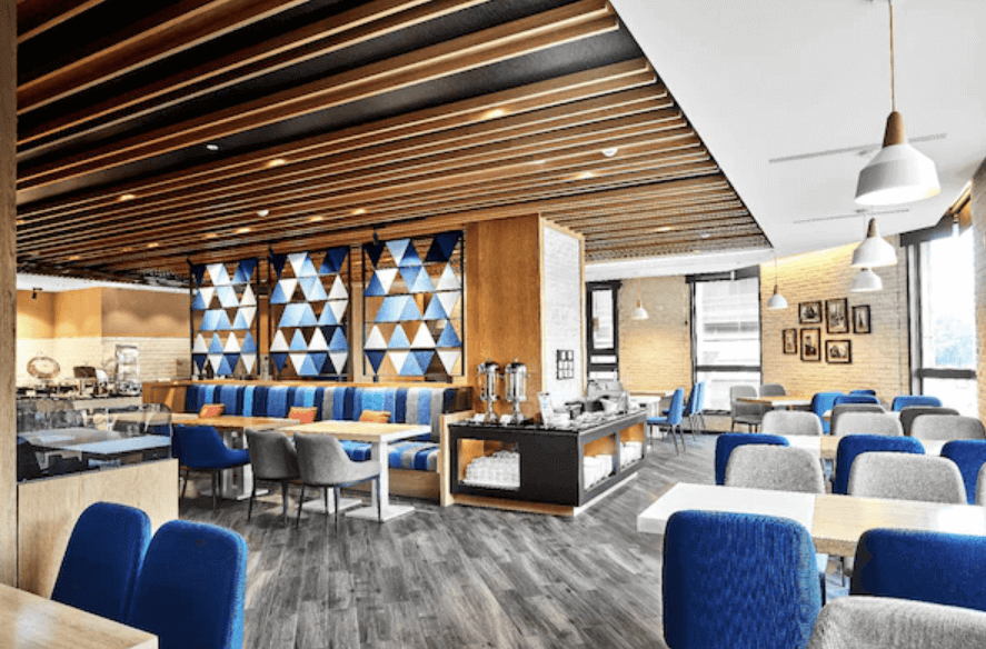 高雄愛河智選假日酒店的餐廳，餐廳內部裝潢現代，採用木質和幾何圖案設計，搭配藍色和灰色的座椅，營造出舒適的用餐環境。餐廳空間寬敞明亮，提供豐富的餐飲選擇，是賓客享用早餐或其他餐點的理想場所