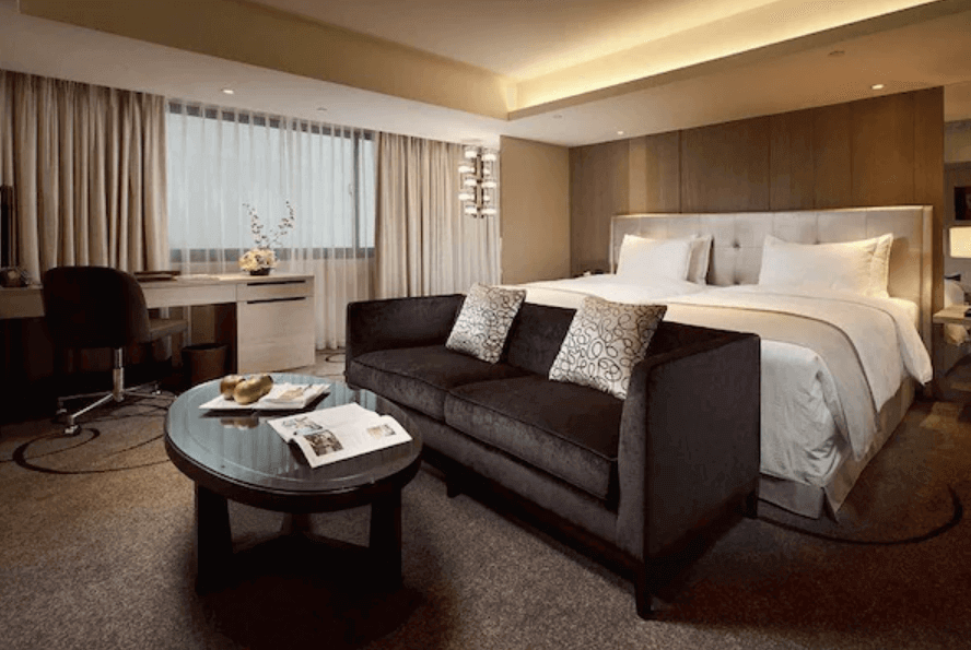 【高雄親子飯店】高雄翰品酒店的豪華雙人房，房間內設有一張大床，配備高品質的床上用品，提供舒適的睡眠環境。房間內還有一張沙發和茶几，讓賓客能夠放鬆休息。窗戶採用落地窗設計，提供充足的自然光，並且房間設有工作區域，方便商務旅客使用。