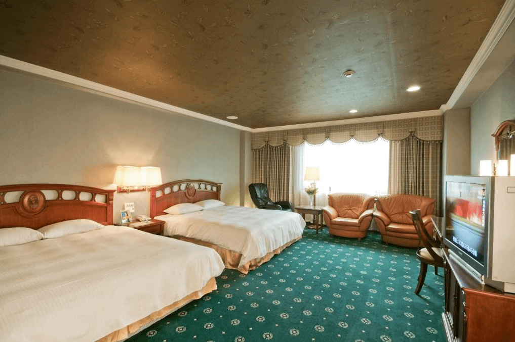 F HOTEL台南館展示了一間寬敞的雙床房。房間內有兩張大床,床頭板設計古典。房間內有一個寬敞的休息區,配有舒適的沙發椅和茶几,為家庭旅客提供足夠的活動空間。地毯和天花板的圖案與房間的整體裝潢風格相匹配