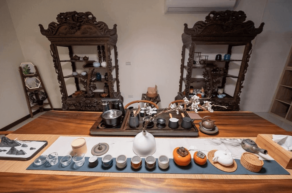 千柏旅居展示了一個傳統茶具展示區。桌上擺放著各種精美的茶具,背景牆上有兩個雕花木製書架,擺放著各式各樣的茶壺和茶杯。這個區域充滿了傳統的中式風格,給人一種寧靜和雅致的感覺。