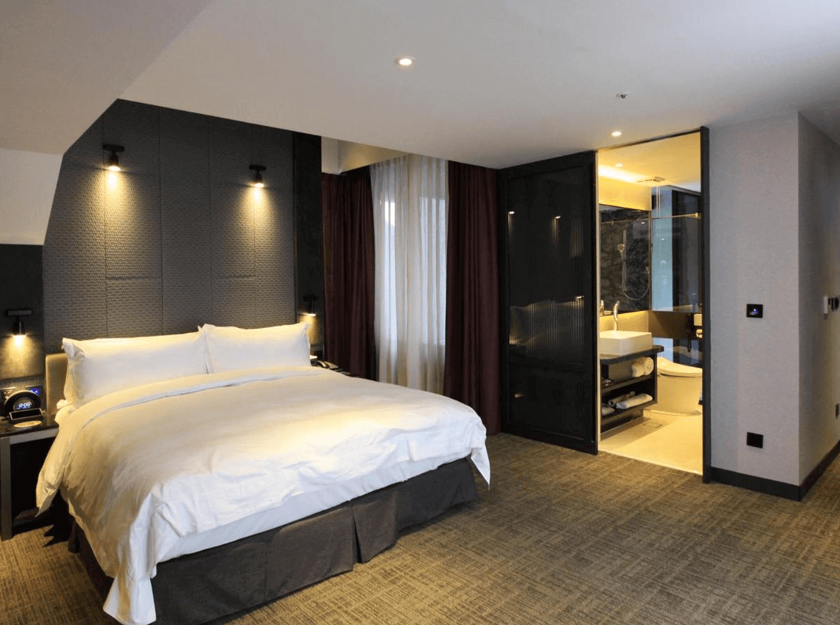 天閣酒店-台北劍潭館展示了一間溫馨的大床房。房間內設有一張大床，床頭牆是深色的，營造出溫暖而安靜的氛圍。房間還連接了一間現代化的浴室，提供了方便的住宿體驗。