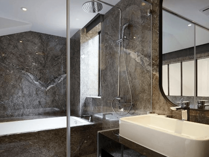 天雲旅棧-台北基河展示了一間豪華的浴室。浴室內有一個寬敞的淋浴區，裝有現代化的花灑。淋浴區旁邊是一個大型的浴缸，適合放鬆泡澡。浴室內牆壁和地板都採用了深色大理石材質，顯得非常高雅和現代。洗手台上擺放著一個方形的洗手盆，整體設計簡約大方。