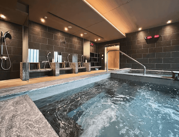 見潭璞旅的溫泉浴場，浴場內有幾個淋浴區和一個大熱水池。牆壁是深色的石材裝飾，設有木製凳子，環境舒適且設計現代。