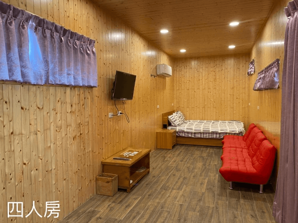 鎮安粉紅豹的四人房內部,房間採用木質牆壁和天花板設計,充滿自然氣息。房間內有一張大床、一張紅色沙發和一台掛牆電視,整體感覺溫馨且舒適。