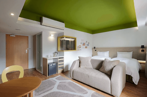 陽光士林珮柏旅館展示了一間裝飾現代的酒店客房。房間內有兩張單人床，床上鋪著白色的床單，顯得非常乾淨舒適。房間的天花板是明亮的綠色，與白色的牆壁形成對比。房間內還有一個沙發，適合放鬆和休息。整體設計簡約溫馨，讓人感覺非常舒適。