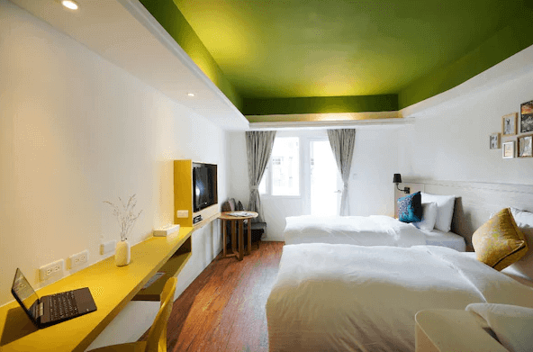 陽光士林珮柏旅館展示了一間現代風格的酒店客房。房間內有兩張大床，床上鋪著白色的床單，顯得非常乾淨舒適。房間內部採用明亮的綠色天花板，白色牆壁和木地板。房間內有一個小桌子和椅子，適合工作或休息。整體設計簡約大方，顯得非常現代和舒適。