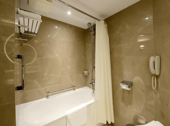 "台北小巨蛋住宿"兄弟大飯店的浴室的圖片，內部採用淺色大理石材質，具有現代感。浴缸設計簡約，配有淋浴設施。牆上設有毛巾架，旁邊還有一部牆上電話，便於使用者在浴室內緊急聯絡。