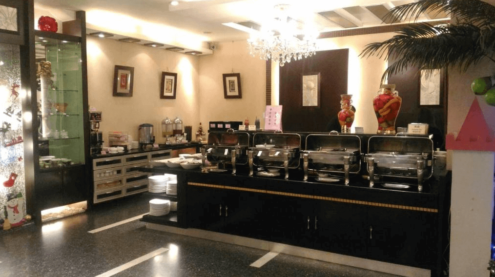 北都大飯店自助餐區的照片，擺放著多個餐盤和餐具，櫃台上方有水晶吊燈，整體氛圍典雅。背景可見各式飲品機和擺盤，周圍有裝飾品增添節日氣氛。