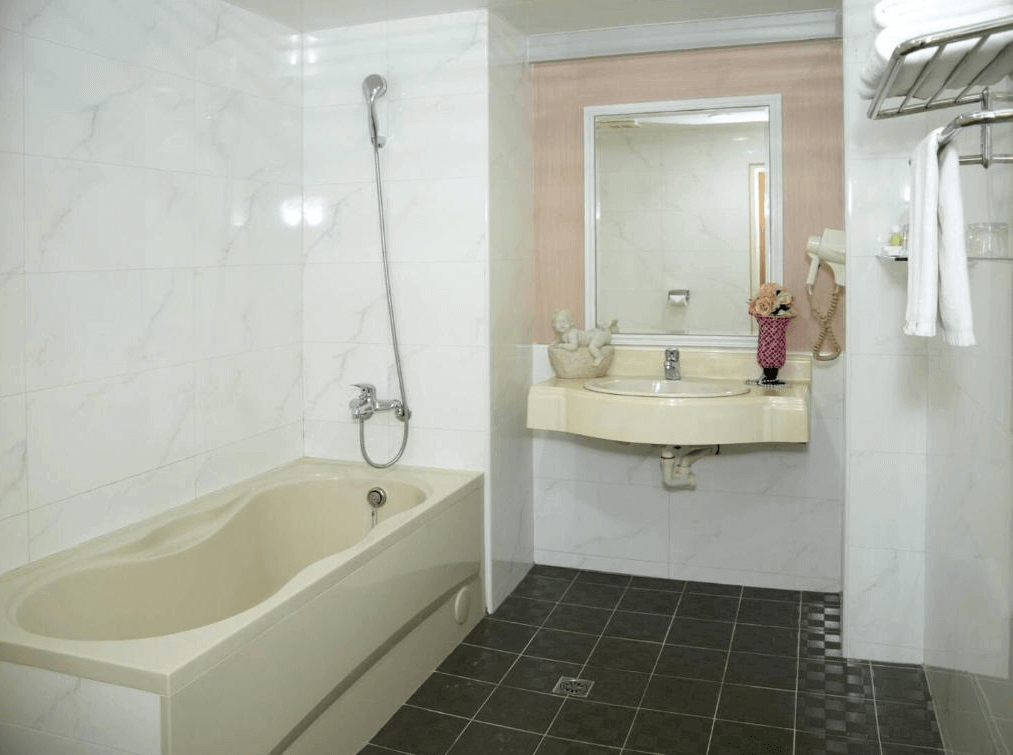 北都大飯店浴室的照片，浴室內有一個大浴缸，牆面和地板採用大理石紋理的瓷磚裝飾。洗手台上方有一面鏡子，旁邊有一個小花瓶裝飾，整體感覺乾淨且舒適。