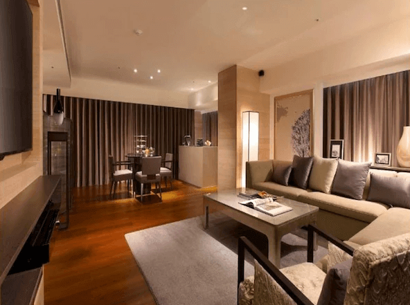 【松山機場住宿】和逸飯店-台北民生館的起居室圖片，設計風格現代且溫暖。房間內設有舒適的沙發和茶几，地板使用木質材料，增添了自然的溫暖感。起居室內還有一個小型餐桌區，空間寬敞，燈光柔和，適合家庭或朋友聚會。