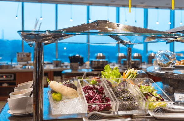 基隆長榮桂冠酒店的自助餐區的照片，展示了擺放在冰塊上的各種新鮮蔬菜和配料，背景可見寬大的落地窗和窗外的美麗景色。