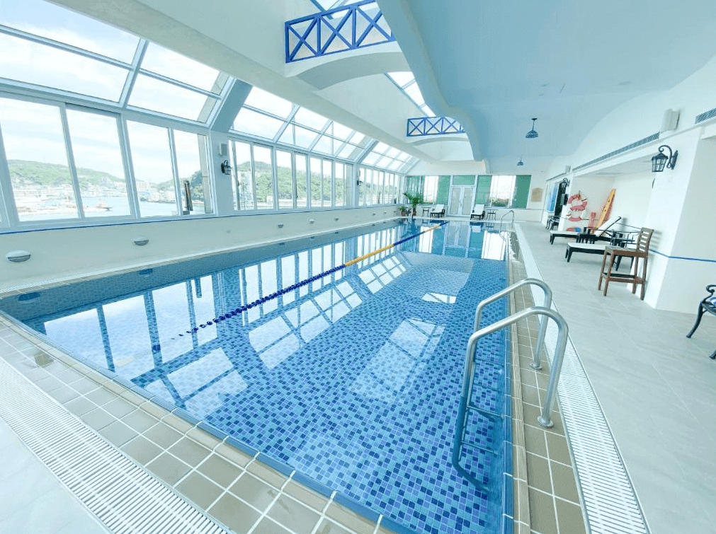 基隆長榮桂冠酒店的室內游泳池的照片，游泳池邊的牆面上有大面積的玻璃窗，可以看到窗外的風景。泳池旁邊放有幾把躺椅和桌椅，環境明亮而舒適。