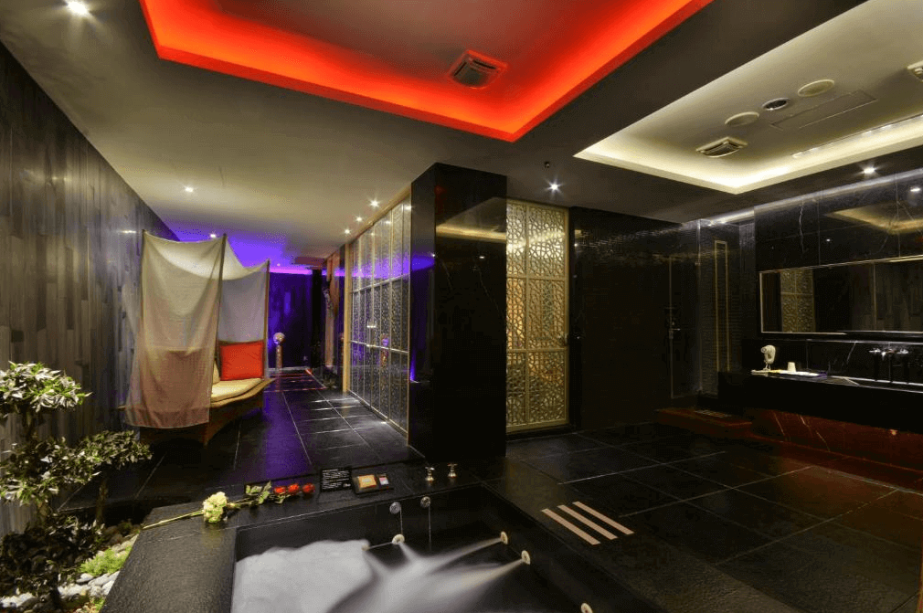 【台中情趣汽車旅館】夏都汽車旅館浴室設計豪華，擁有寬敞的空間和現代化的設施。天花板上的紅色燈光營造出浪漫的氛圍，浴室內的裝飾細節豐富，牆面採用黑色大理石材質，提供了一個高級且放鬆的環境。