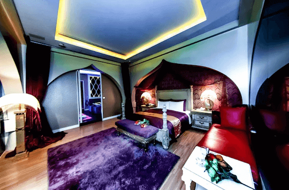 【台中情趣汽車旅館】夏都汽車旅館房間設計充滿異國情調，擁有濃郁的紫色地毯和紅色的床具。拱形的門和牆面的設計讓人彷彿置身於神秘的東方宮殿，燈光設計巧妙，為房間增添了浪漫和神秘感。