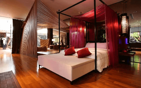 【台中情趣汽車旅館】天月人文休閒汽車旅館房間設計充滿東方風情，四柱床搭配紅色床幔，營造出浪漫和奢華的氛圍。房間內的木質地板和屏風設計增添了溫暖的感覺，提供了一個舒適的休息空間。