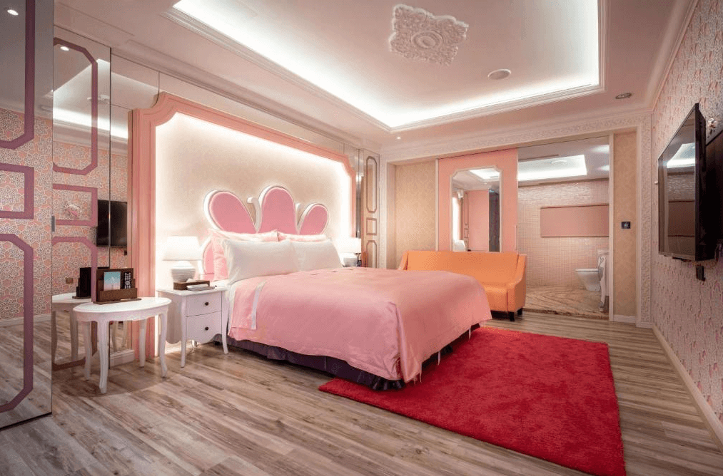 【台中情趣汽車旅館】極光情境旅館房間設計可愛且溫馨，牆面和家具以粉紅色為主，營造出夢幻般的氛圍。床頭板設計成花瓣形狀，增加了房間的童話感。這是個適合浪漫度假或特殊場合入住的理想場所。