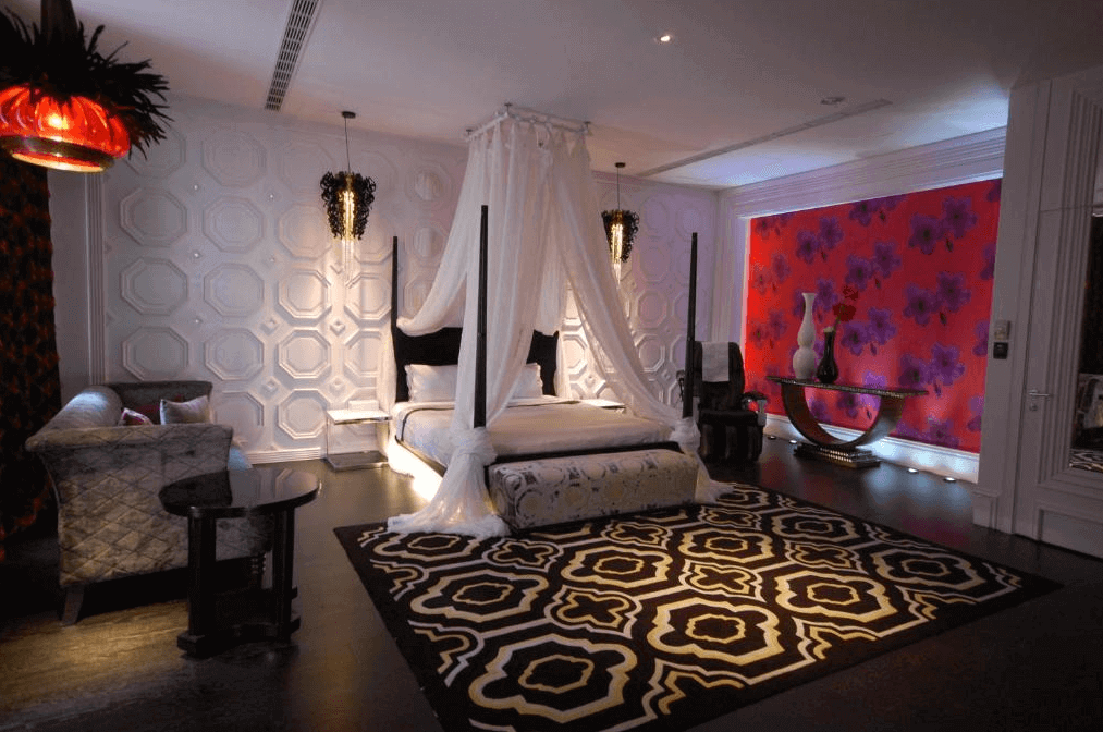 【台中情趣汽車旅館】沐蘭精品旅館台中館房間融合了奢華和現代感，設有一張大床，上方裝飾著優雅的床幔。房間的牆壁上有獨特的幾何圖案裝飾，整體色調以黑白為主，搭配紅色花卉壁紙，營造出高貴典雅的氛圍。設計感強烈的燈具增加了房間的時尚感。