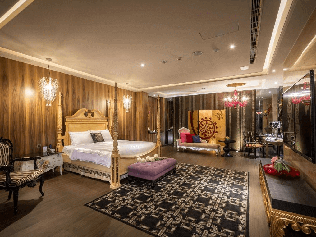 【台中情趣汽車旅館】沐蘭精品旅館台中館房間擁有豪華的裝飾風格，金色的大床和壁紙顯得格外華麗。房間內還有舒適的沙發和獨特的藝術裝飾品，整體氛圍溫暖且高雅。華麗的吊燈和精緻的地毯為房間增添了更多的奢華感。