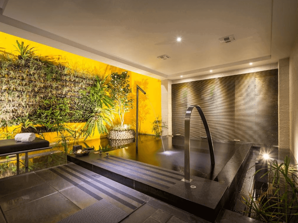 【台中情趣汽車旅館】沐蘭精品旅館台中館浴室設計充滿自然氣息，牆上有綠色植物裝飾，讓人感覺彷彿置身於自然之中。浴室內的黃牆和現代化的浴池設計，使得整體環境既溫馨又放鬆，是一個理想的休息場所。