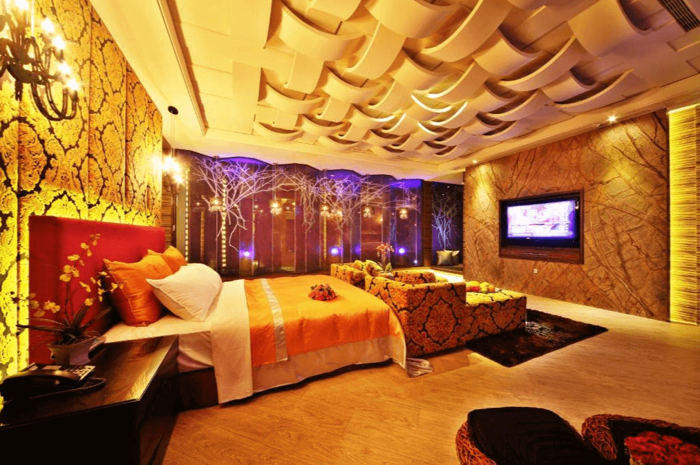 【台中情趣汽車旅館】涵館汽車旅館房間的設計華麗且溫馨，牆面覆蓋著金色花紋壁紙，搭配鮮豔的紅色床頭板。天花板上有獨特的裝飾設計，營造出富有層次感的視覺效果。房間內的燈光柔和，讓人感到舒適放鬆。