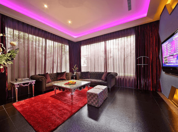 【台中情趣汽車旅館】涵館汽車旅館的起居室設計現代且奢華，擁有大面積的落地窗，窗外景色宜人。天花板上的紫色燈光和窗簾相呼應，增添了房間的浪漫氛圍。舒適的沙發和時尚的裝飾讓這個空間既適合休息也適合娛樂。