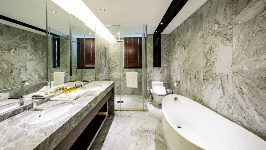 "台北小巨蛋住宿"甲山林湯旅的豪華浴室圖片，內部裝潢以灰色大理石為主，顯得非常高級。浴室配有一個獨立式的白色浴缸，淋浴間由透明玻璃隔開，雙人洗手台上擺放著高品質的衛浴用品，整體設計非常講究，營造出舒適且奢華的沐浴環境。