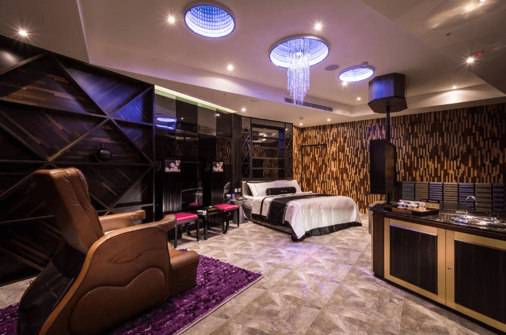 【台中情趣汽車旅館】紫禁城MOTEL主題會館房間設計寬敞且現代，配有舒適的大床和按摩椅。房間內的燈光設計精緻，天花板上的水晶吊燈增添了奢華感。牆面裝飾著木質和金屬元素，營造出時尚且溫馨的氛圍。