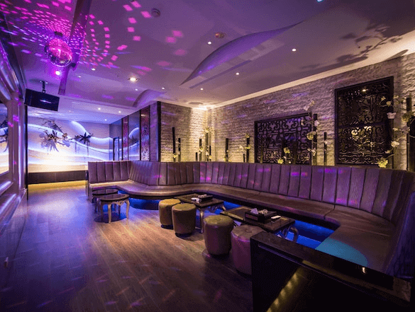 【台中情趣汽車旅館】紫禁城MOTEL主題會館房間設有寬敞的休息區，長形沙發圍繞著中央的桌子，適合多人聚會。燈光設計營造出溫馨且輕鬆的氛圍，牆上的裝飾細節豐富，讓整個空間既時尚又舒適。這是個適合休閒放鬆的理想場所。