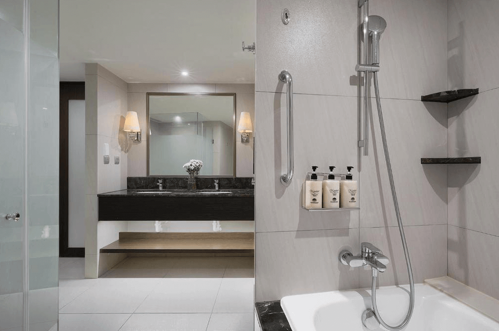 "台北小巨蛋住宿"茹曦酒店的浴室，內部裝潢以淺色瓷磚為主，營造出乾淨且明亮的氛圍。浴缸配有淋浴設施，牆上設有洗浴用品，擺放整齊。浴室內還配有一個雙人洗手台，設計簡約實用，給人一種清新舒適的感覺。