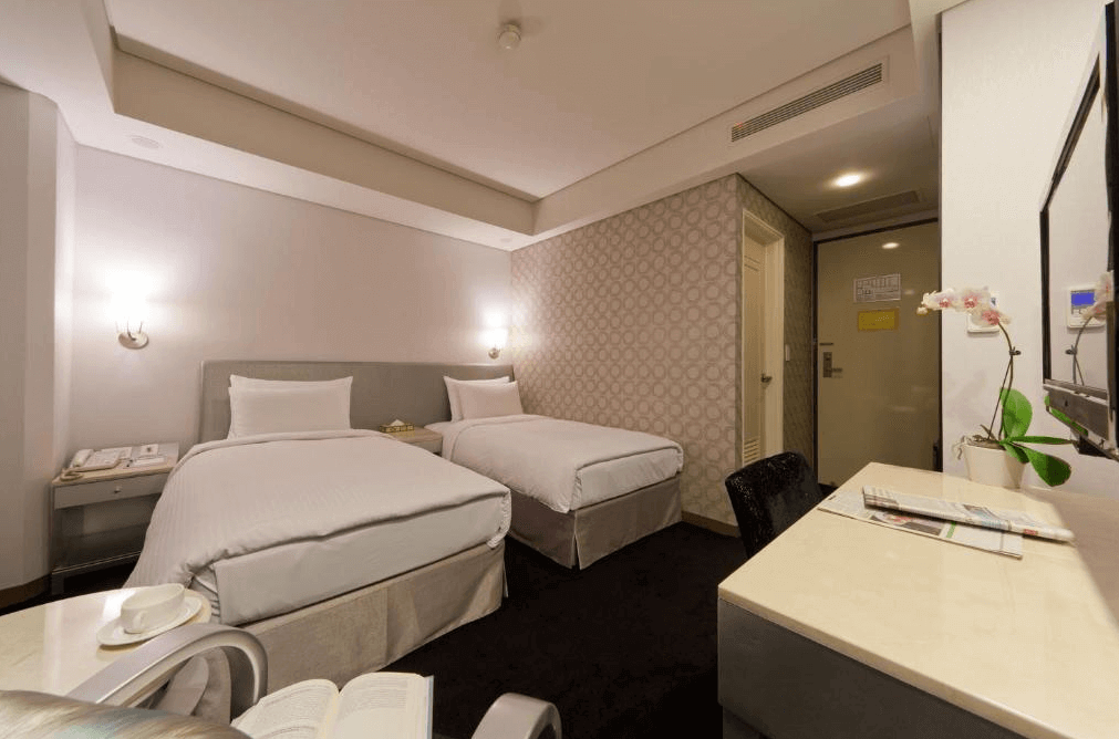 華帥海景飯店雙床房的照片，房間內有兩張單人床，床頭背景牆為淺灰色，牆上安裝了兩盞床頭燈，房間內還設有一張書桌和一面大鏡子，設計簡約，氛圍溫馨。