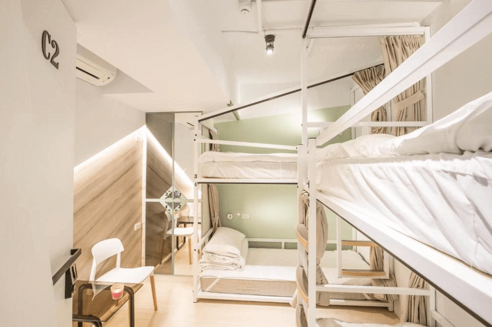宿舍式房間內部照片，房間內有兩個上下鋪的床位，床位之間設有布簾以提供隱私。牆上裝有鏡子，旁邊放置了一張小椅子，整體設計明亮且實用。